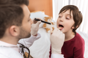 Man doctor examining throat of little boy in hospital