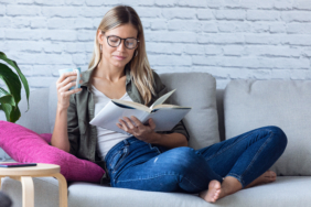 Pretty young woman reading a book and drinking a cup of coffee w